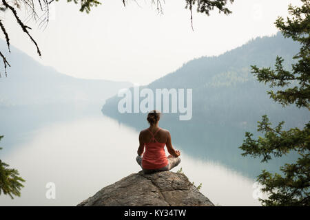 Montare donna seduta nella postura meditando sul bordo di una roccia Foto Stock