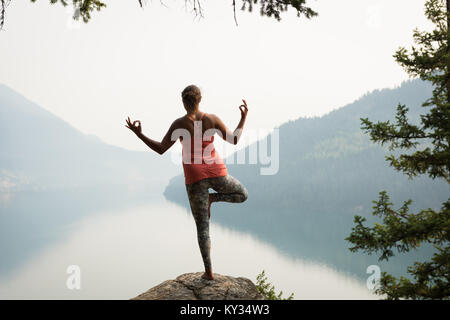 Montare la donna in equilibrio su una gamba sul bordo di una roccia Foto Stock