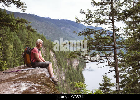 Donna matura rilassante sulla roccia e guardando a vista Foto Stock
