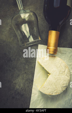 Francese morbido formaggio Camambert con taglio fuori cuneo sulla carta pergamena bianca vetro vuoto bottiglia di vino sulla pietra scuro dello sfondo. Vista superiore piatta copia laici Spac Foto Stock