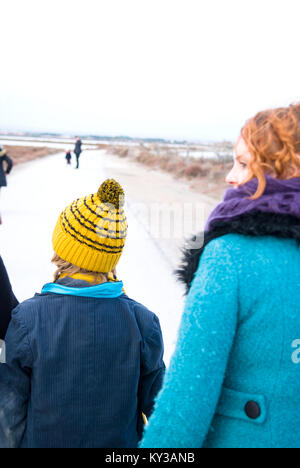 Una madre con orange dei capelli ondulati cammina accanto a suo figlio con un giallo stripey wooly hat. A distanza di un padre e figlio attendono Foto Stock