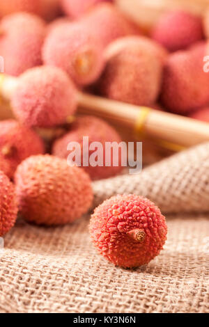 Studio shot con frutti (Lichi) del litchi tree (Litchi chinensis) su grossolana del sacco di tessuto con un singolo bruscamente frutta figurato in primo piano Foto Stock