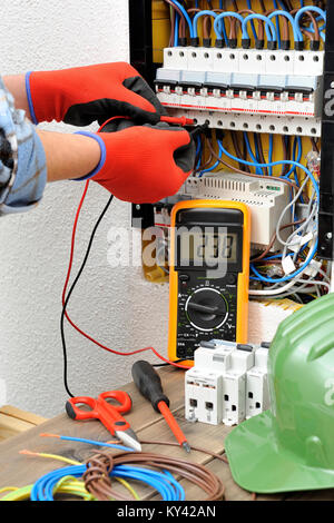 Giovane tecnico elettricista misure con un multimetro la tensione in un quadro elettrico Foto Stock