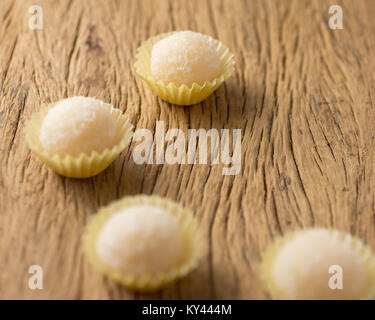 Beijinho è una caramella fatti a mano provenienti dal Brasile. Realizzato con latte condensato e cocco. Bambini festa compleanno dolce. Messa a fuoco selettiva. Tavola in legno rustico. Foto Stock