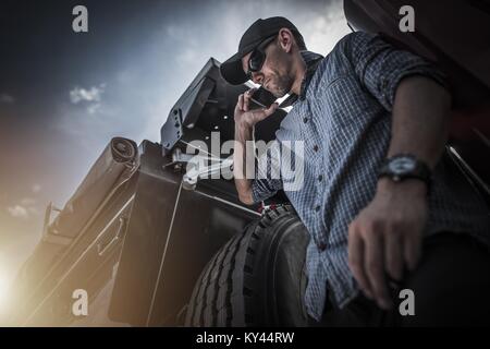 Industria dei Trasporti Business. Caucasian Semi Camionista nella sua 30s a parlare con il cliente al telefono mentre posti a sedere sul suo carrello. Telefono azienda Foto Stock