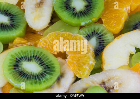Close-up di fettine di kiwi e arance su una macedonia di frutta dello sfondo. Verde e giallo texture dalla succosa blend fruttato pieno di vitamine. Foto Stock