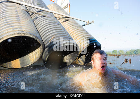 Sussex, Regno Unito. Un giovane uomo tira un viso sconvolto come egli emerge da una piscina di acqua di congelamento durante una dura Mudder ostacolo corso. Foto Stock