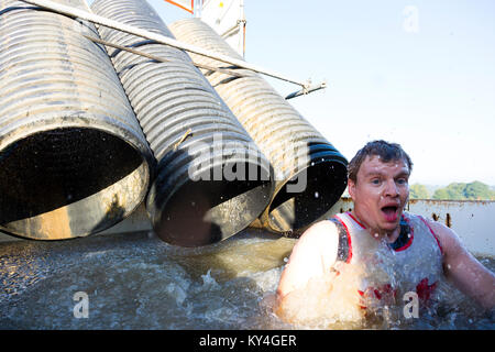 Sussex, Regno Unito. Un giovane uomo tira un viso sconvolto come egli emerge da una piscina di acqua di congelamento durante una dura Mudder ostacolo corso. Foto Stock