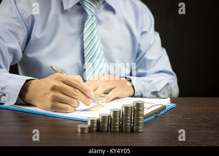 Imprenditore iscritto con impilati di monete di denaro sul tavolo di legno Foto Stock