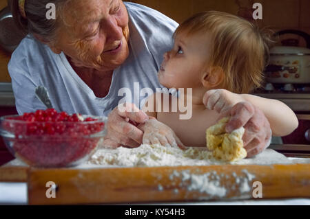 Ritratto di volti, mani felice grey-haired granny, nipote. toddler girl gioca con la cottura, pasta di farina con cucina. bambino baby provare la cucina di studio Foto Stock