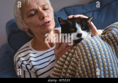 Senior donna seduta su un divano mentre accarezzare il suo gatto di casa Foto Stock