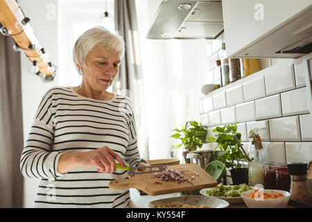 Senior donna aggiunta di cipolle tagliate in una ciotola Foto Stock