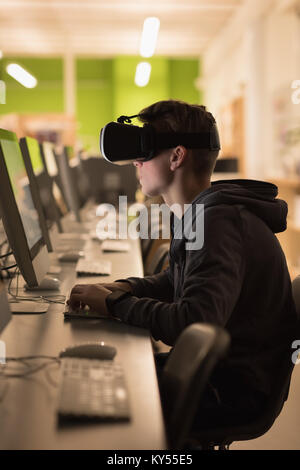 Ragazzo adolescente utilizzando la realtà virtuale cuffie mentre studiano in classe computer Foto Stock