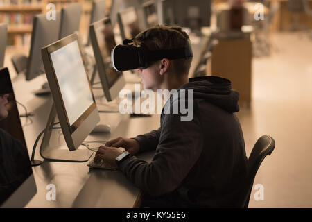 Ragazzo adolescente utilizzando la realtà virtuale cuffie mentre studiano in classe computer Foto Stock