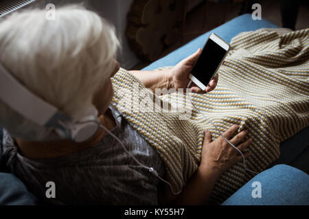 Senior donna ascoltando musica in cuffia mentre si utilizza il telefono cellulare Foto Stock