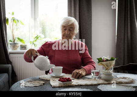 Senior donna versando il tè in tazza da tè pentola Foto Stock