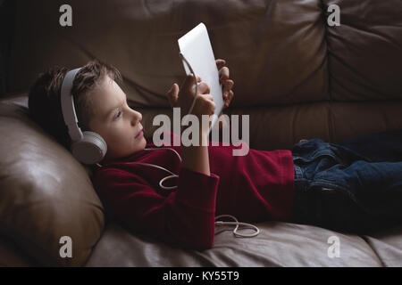 Ragazzo con tavoletta digitale con le cuffie in salotto Foto Stock