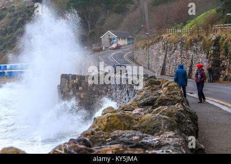 I passanti da guardare la violazione delle onde del mare a parete Meadfoot Beach in Torquay, Torbay, Devon, Regno Unito. Gennaio 2018. Foto Stock
