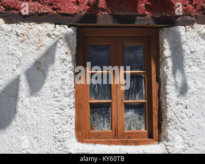 Vecchio in legno finestra con vetri di piccole dimensioni sul muro bianco di un rustico Tibetan House, ombre dalle bandiere di preghiera sulla superficie. Foto Stock