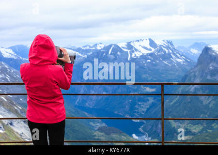Turismo Viaggi e vacanze. Donna che guarda attraverso visite binocolo telescopio turistica, si affaccia il Geirangerfjord e montagne paesaggio dal D Foto Stock