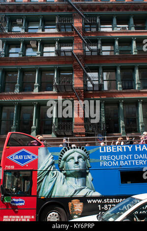 Tour bus con turisti visite turistiche e la facciata di un edificio con scale di emergenza con corrimano delle scale antincendio nella città di New York, New York. Manhattan Foto Stock