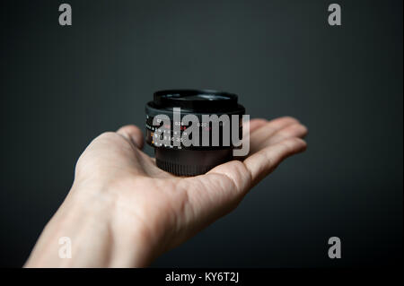 Mano d'uomo in possesso di un obiettivo della telecamera su uno sfondo nero Foto Stock