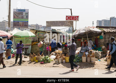 Varie bancarelle con verdure in secchielli per la vendita sul ciglio della strada con la gente che camminava passato, Nairobi, Kenya, Africa orientale Foto Stock