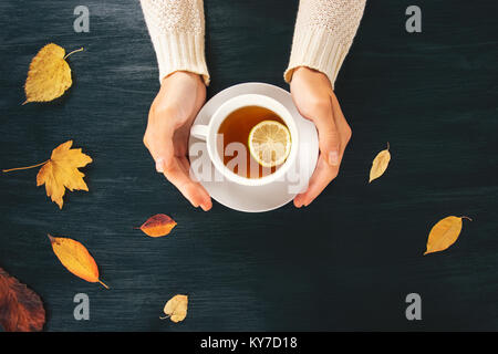 Donna mani tenendo il tè caldo tazza limone sul tavolo di legno con foglie di autunno concetto stagionale vista dall'alto uno stile alla moda Foto Stock