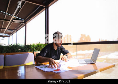 Lavoratore di ufficio ordinamento di carte sul tavolo vicino al computer portatile. Foto Stock