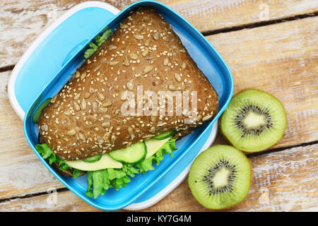 Pranzo sano scatola contenente formaggio marrone rotolo con lattuga e due metà di kiwi Foto Stock