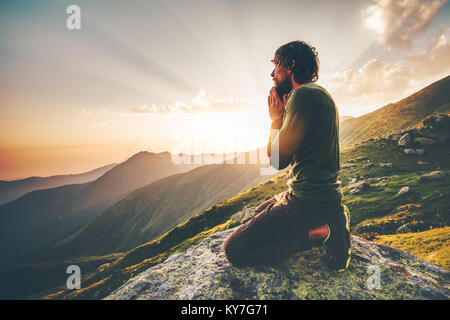 Uomo che prega al tramonto montagne stile di vita viaggio rilassamento spirituale concetto emozionale vacanze outdoor in armonia con la natura Foto Stock