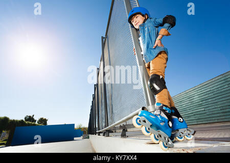 Vista dal basso del ritratto di preteen boy, inline skater in abbigliamento protettivo, in piedi a skate park a giornata di sole Foto Stock