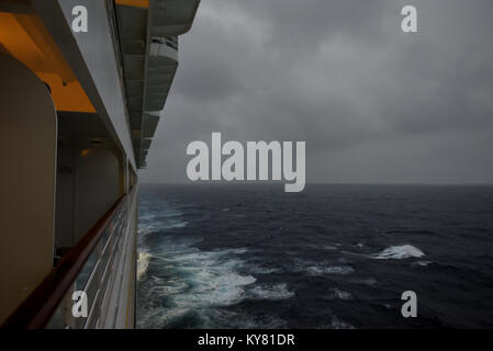 Un balcone vista guardando dietro una nave da crociera come vele sotto grigio / tempestoso cieli nuvolosi nell'Oceano Atlantico voce verso le isole dei Caraibi Foto Stock