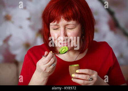 Glamour giovane donna mangiare kiwi e strizzare gli occhi dal piacere. Che piacere di mangiare questa succosa, mature e frutti sani. Foto Stock