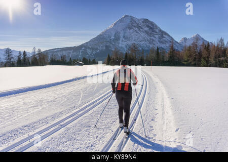 Cross-country sciatore in giacca rossa viene eseguito su piste pista di sci nella soleggiata giornata invernale. In inverno il paesaggio di montagna: Tirolo, Alpi, Austria. Foto Stock