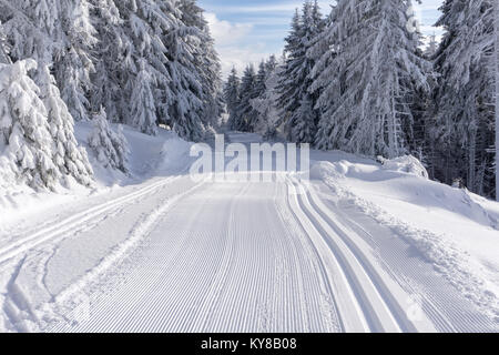 Battute di pista di sci nella soleggiata giornata invernale sui monti road. Alberi coperti di brina e neve fresca illuminata dal sole, nuvole sul cielo blu. Foto Stock