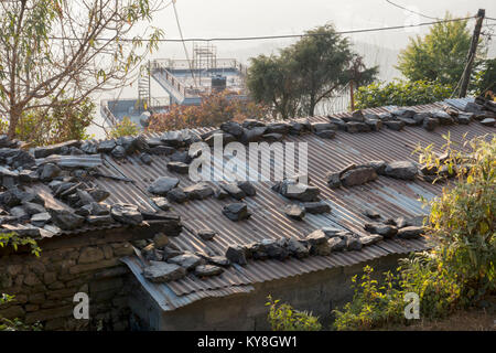 Ferro corrugato per copertura di semplici abitazioni tenuto premuto con grandi pietre, in Sarankot, Nepal Foto Stock