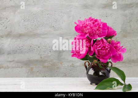 Bouquet di peonie rosa in una caraffa in ceramica sulla luce di un tavolo in legno con uno sfondo sfocato Foto Stock