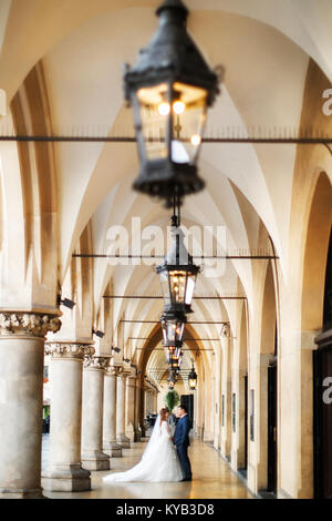 Sposi novelli in piedi tra le colonne dell'antico edificio. Fila di lampade stradali. Foto Stock