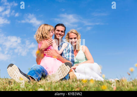 Famiglia seduta in erba verde sul prato Foto Stock