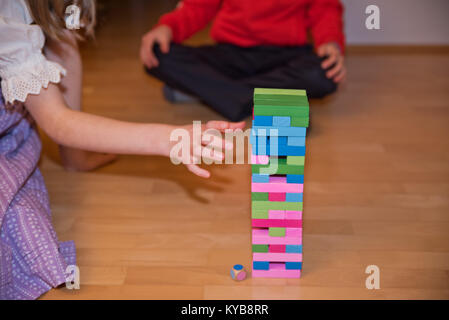 Ragazza cercando di estrarre un componente di un colorato Jenga aka Klodsmajor tower Foto Stock