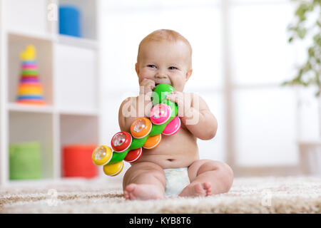 Carino il bambino nel pannolino si siede sul tappeto e gioca con il giocattolo a casa. Profondità di campo. Foto Stock