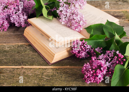 La composizione della fioritura di rami di lilla e libro aperto su un sfondo di legno leggera profondità di campo a. Foto Stock