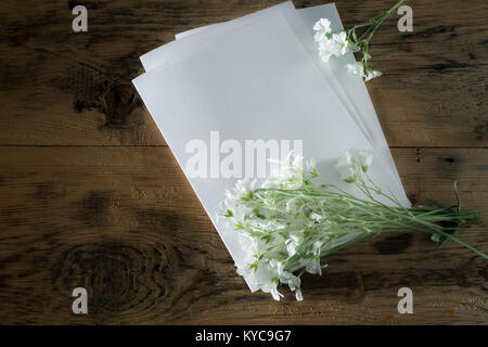 Composizione con un foglio di carta bianco e un piccolo bouquet di fiori bianchi su uno sfondo di legno. Tonica foto Foto Stock