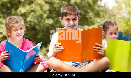 Dei bambini felici di tre seduti sul prato con libri Foto Stock