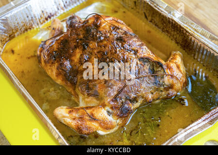 Spiedo di pollo arrosto con i suoi grassi in un contenitore metallico Foto Stock