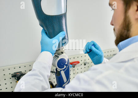 Ritratto di protesi tecnico rendendo protesi di gamba seduto alla scrivania in laboratorio moderno, il controllo di qualità e di effettuare le regolazioni Foto Stock