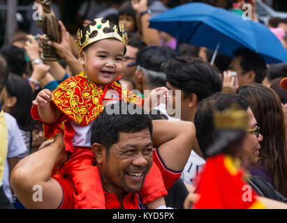 Cebu City, Filippine. 14 gennaio, 2018. Un sorridenti bambino vestito di un Santo Nino vestito come egli siede sui suoi padri spalle.come parte di Il Sinulog 9 giorni di festa religiosa,i cattolici filippini si riuniscono per la mattina presto la messa domenicale portando con loro Santo Nino figurine,repliche di Gesù bambino.La credenza in questa effige risale al tempo di explorer Ferdinand Magellan che ha dato la statuetta originale come un dono quando ha atterrato nel 1521 a Cebu. Credito: galleria immagini2/Alamy Live News Foto Stock