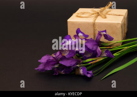 Bouquet di fiori viola iridi e dono su uno sfondo nero. profondità di campo Foto Stock