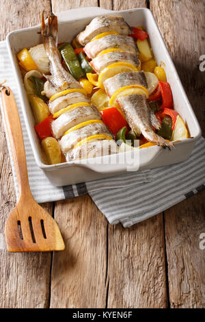 Merluzzo bianco Pesce al forno con pepe, pomodori, cipolle e limone in una teglia close up su una tavola verticale. Foto Stock